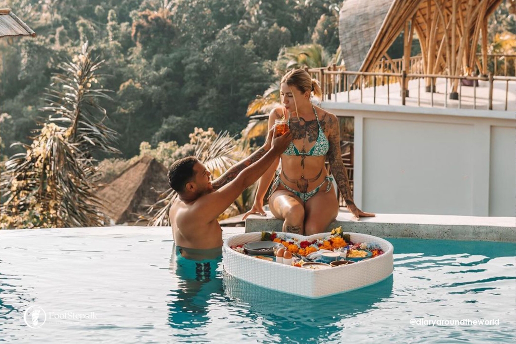 Thing not to do in Bali - A couple enjoys a floating breakfast in a pool with a scenic lush backdrop at Bali